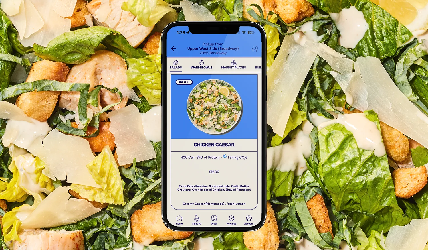 Smartphone displaying a Chicken Caesar salad menu with nutrition info and ingredients over a background of fresh Caesar salad with lettuce, chicken, croutons, and shaved Parmesan.