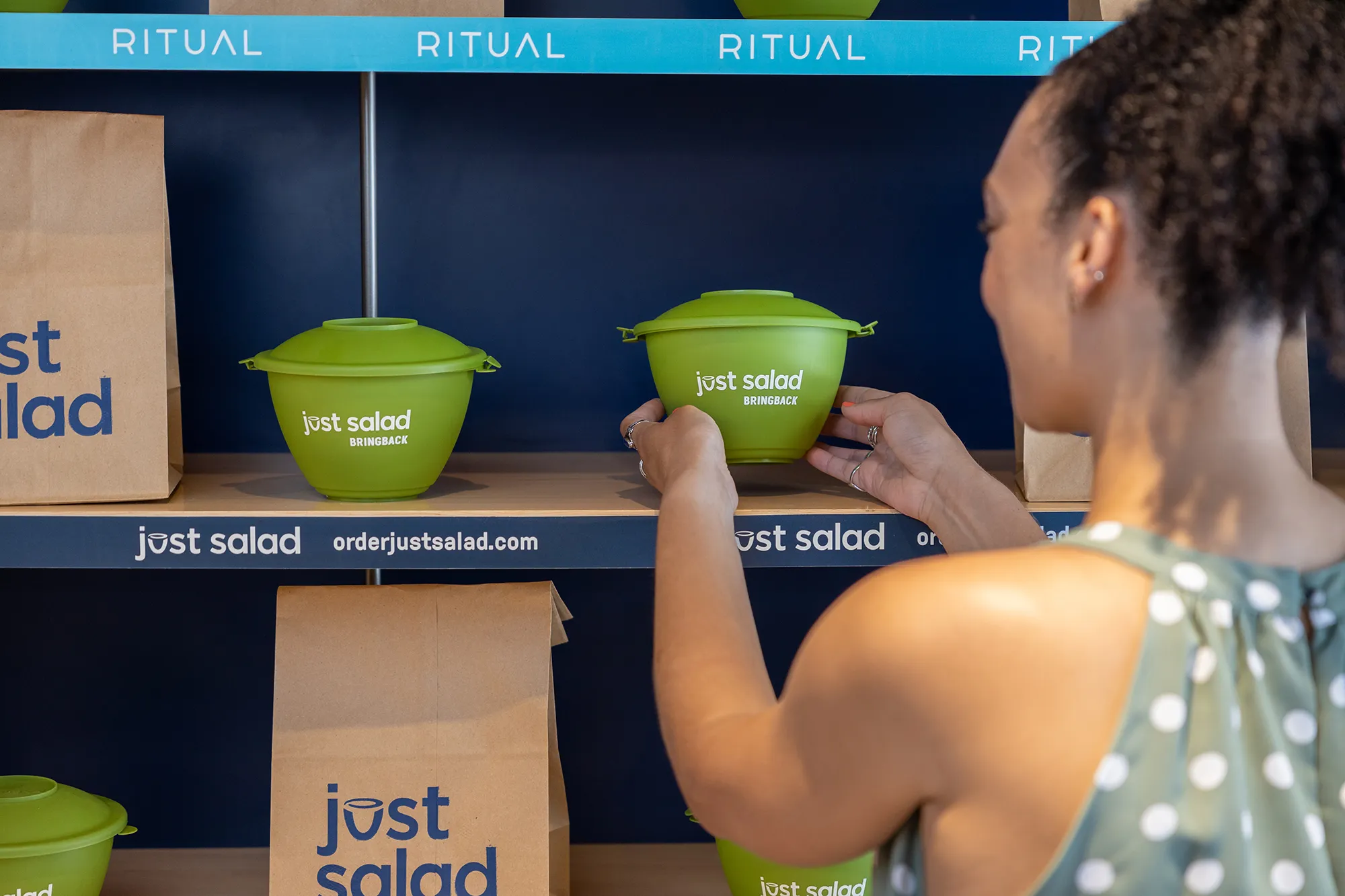 A person picking up a Just Salad BringBack bowl from the counter.