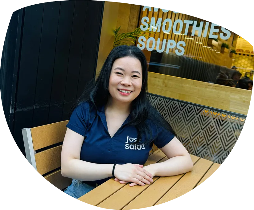 Smiling woman with long dark hair wearing a navy shirt sitting at a wooden table outside a café.
